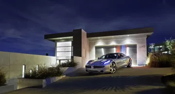 Fisker Karma aparcado frente a una casa contemporánea, iluminación nocturna.
