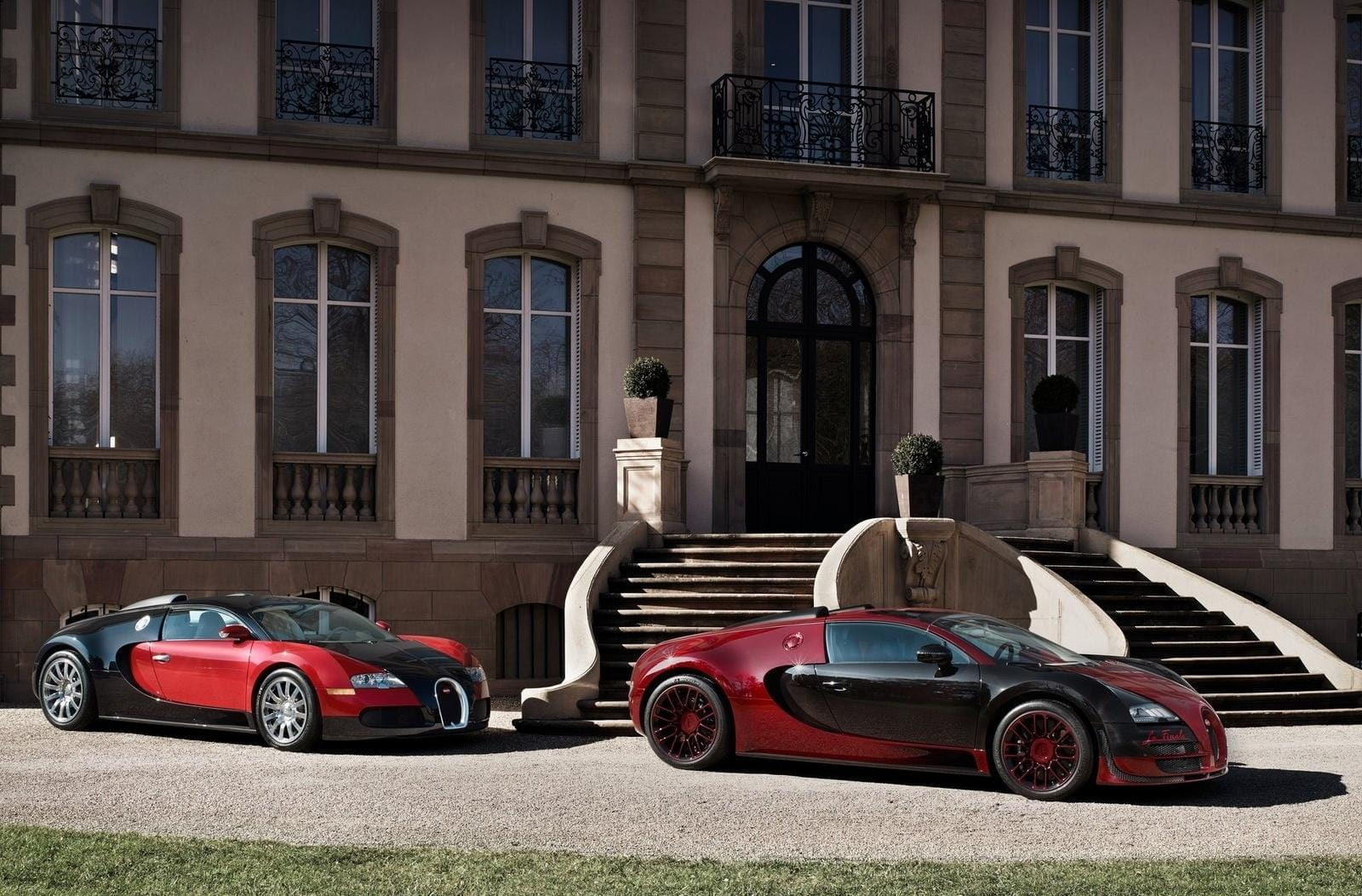 Dos Bugatti Veyron posan lateralmente frente a una elegante mansión.