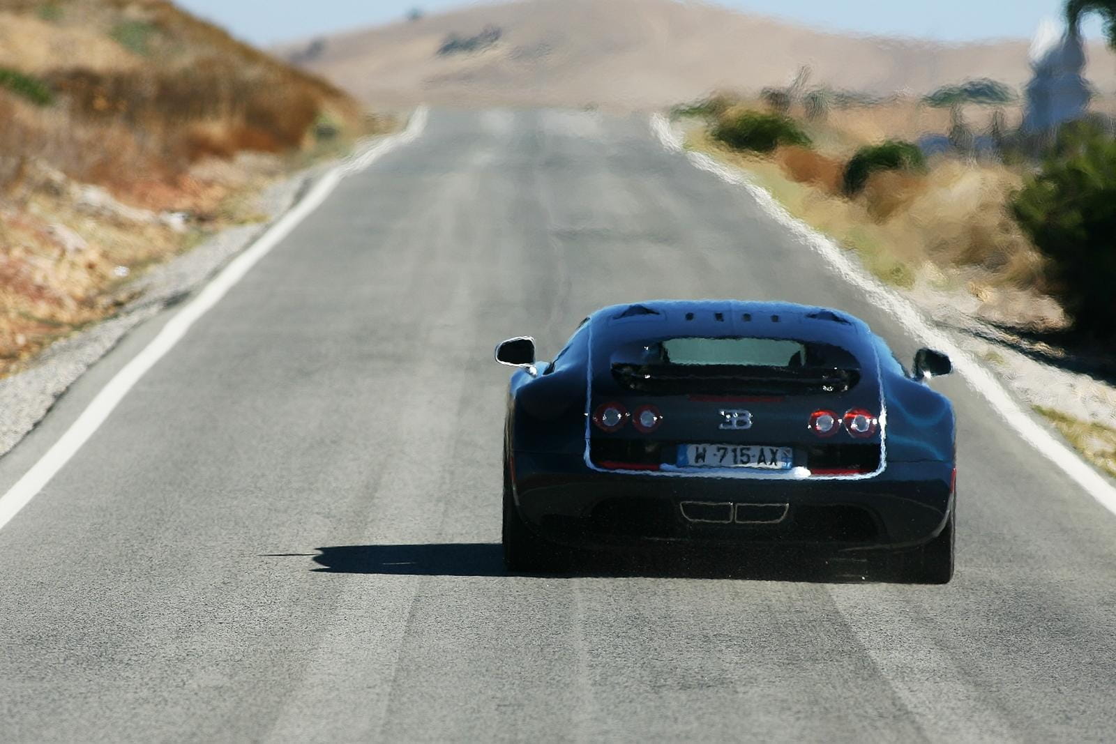 Vista trasera del Bugatti Veyron en carretera, destacando su aerodinámica.
