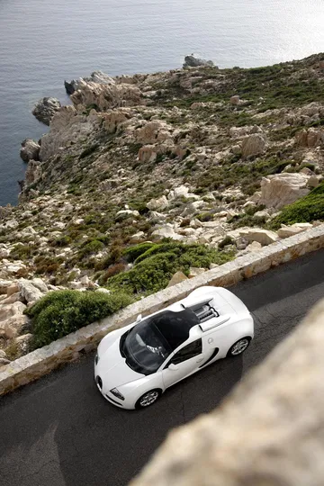 Vista aérea de un Bugatti Veyron blanco con el techo abierto rodando cerca de la costa.