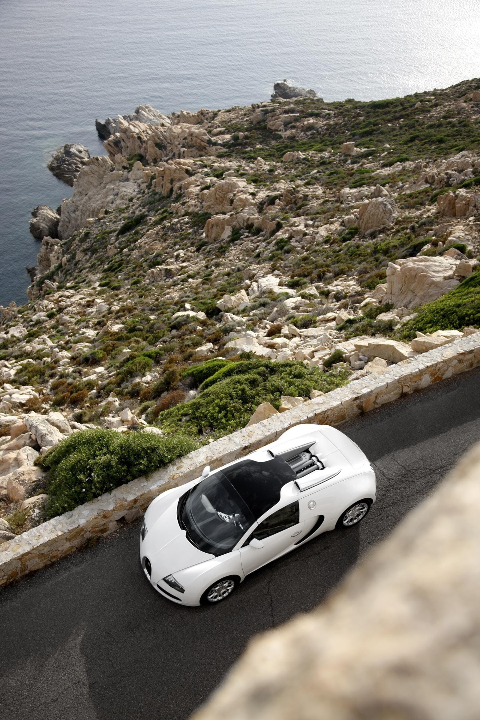 Vista aérea de un Bugatti Veyron blanco con el techo abierto rodando cerca de la costa.