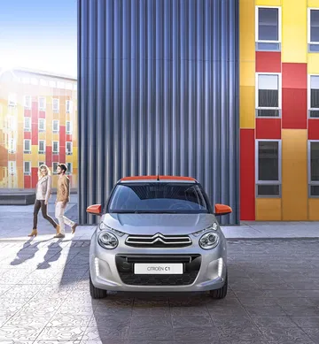 Vista frontal del Citroën C1 aparcado en un escenario urbano, destacando su diseño compacto.