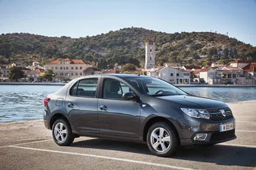 Vista lateral del Dacia Logan aparcado con vista al puerto.
