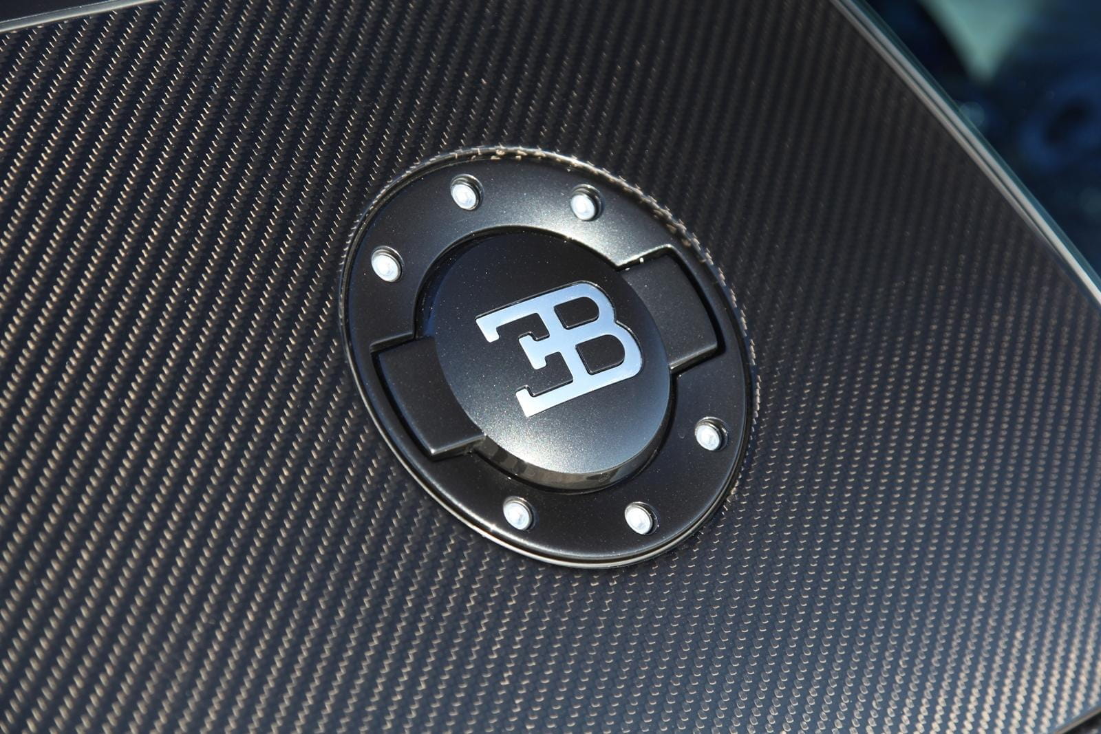 Primer plano del emblemático emblema de Bugatti en textura de fibra de carbono.