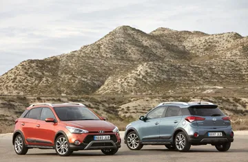 Vista en perspectiva de dos Hyundai i20, uno rojo y otro azul, con fondo montañoso.