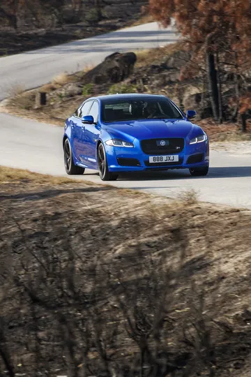 Vista dinámica del Jaguar XJ en carretera, enfatizando su frontal y perfil lateral.