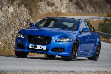 Vista dinámica del Jaguar XJ en una carretera de montaña, destacando su frontal y perfil