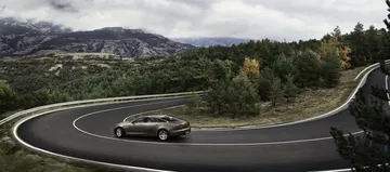 Vista lateral de un Jaguar XJ en una carretera de montaña, destacando su elegante diseño.