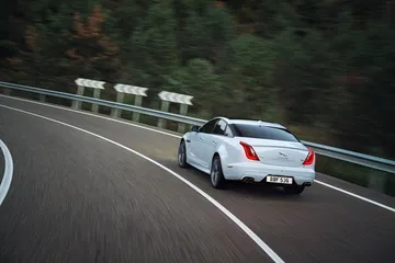 Vista dinámica del Jaguar XJ en carretera, enfatizando su elegante diseño trasero.