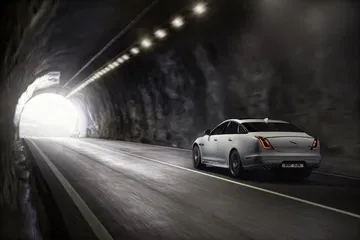 Jaguar XJ proyectando elegancia y poder en un túnel iluminado, vista lateral y trasera.