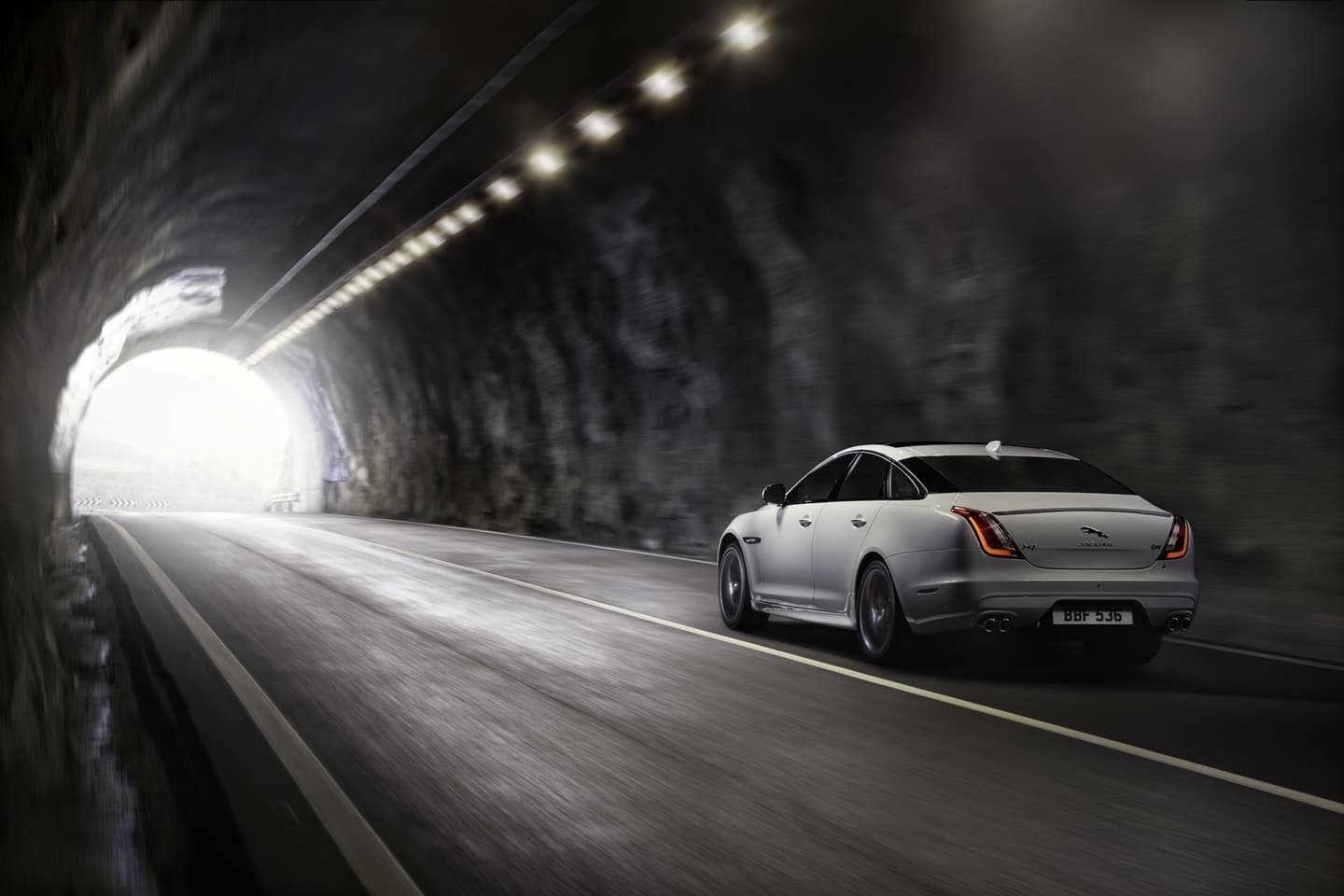 Jaguar XJ proyectando elegancia y poder en un túnel iluminado, vista lateral y trasera.