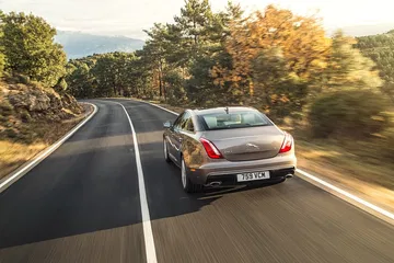 Vista dinámica de un Jaguar XJ desde la perspectiva trasera lateral en carretera.
