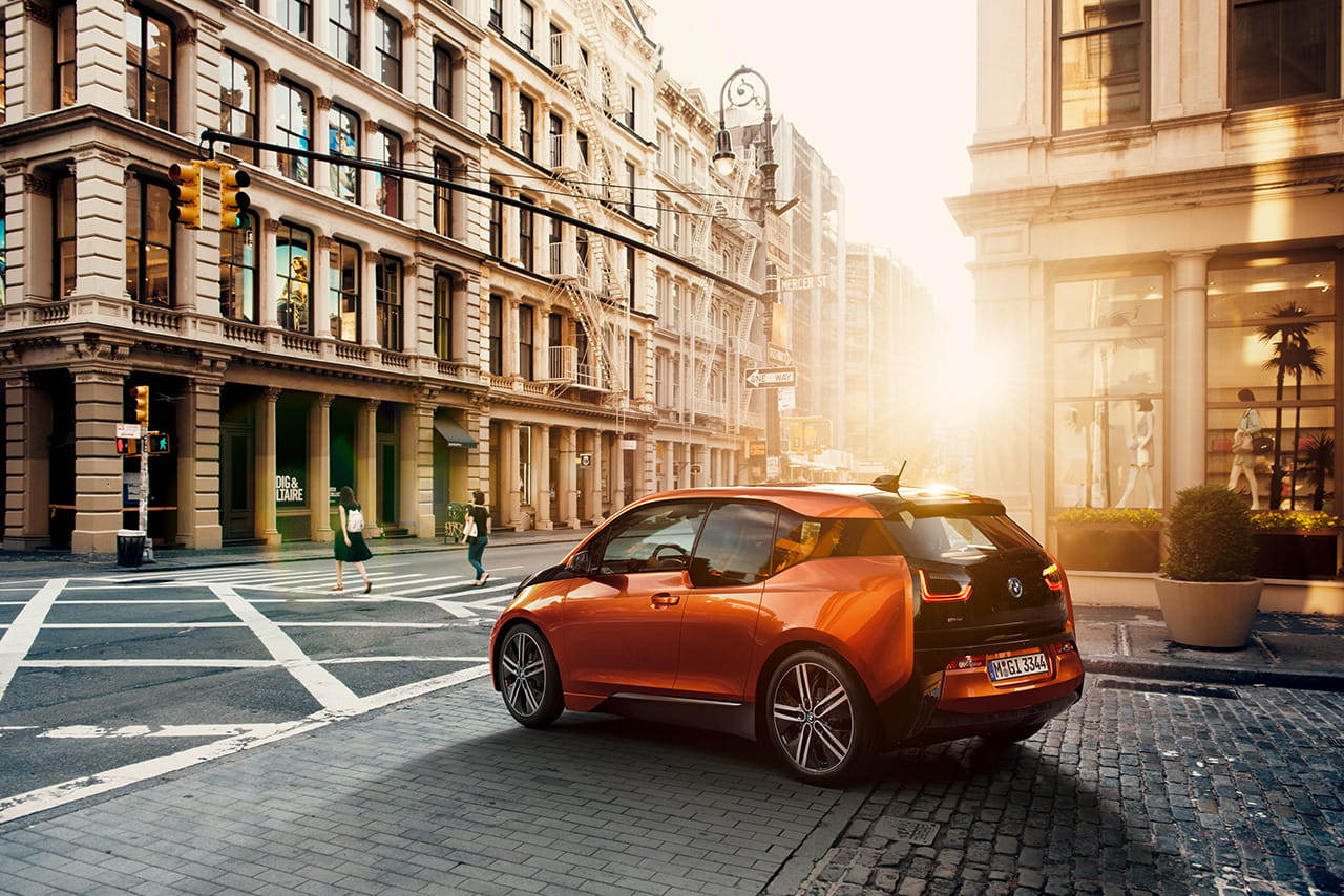 Vista lateral trasera del BMW i3 en un entorno urbano con iluminación solar.