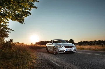 BMW Serie 2 Cabrio capturado al atardecer sobre asfalto, luces y parrilla visibles.