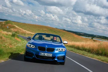 Vista dinámica del BMW Serie 2 Cabrio, azul, en carretera abierta.