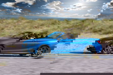 Vista lateral del BMW Serie 2 Cabrio con capota bajada en escenario costero.