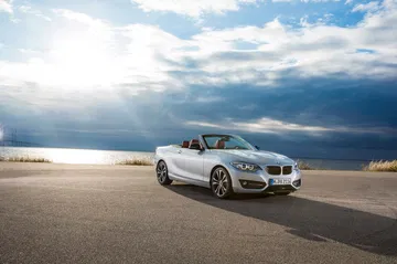 Vista dinámica del BMW Serie 2 Cabrio con capota bajada y cielo nublado.