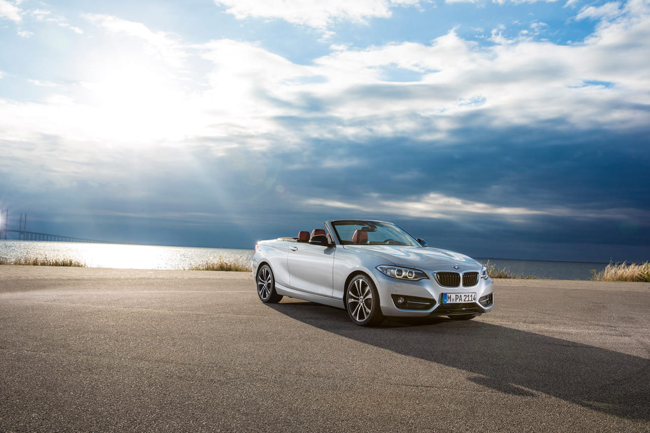 Vista dinámica del BMW Serie 2 Cabrio con capota bajada y cielo nublado.