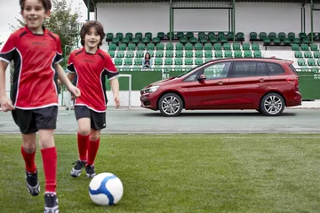 Vista lateral del BMW Serie 2 Gran Tourer en un campo de fútbol, color rojo.