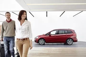 Vista lateral del BMW Serie 2 Gran Tourer en color rojo, acompañado de dos personas.