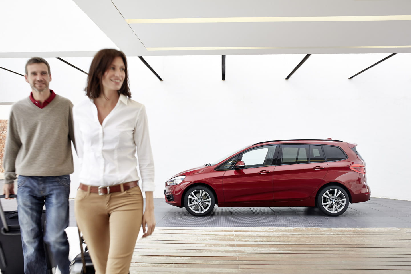 Vista lateral del BMW Serie 2 Gran Tourer en color rojo, acompañado de dos personas.