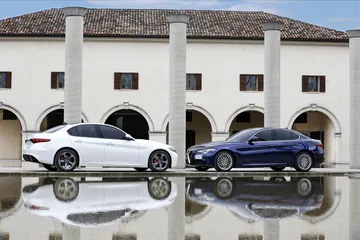 Vista lateral de dos Alfa Romeo Giulia, uno blanco y otro azul, reflejados sobre una superficie pulida.