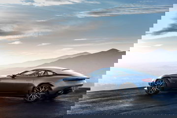 Vista lateral del Aston Martin DB11 posando sobre asfalto con montañas al fondo.