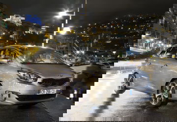 Kia Carens iluminado por la ciudad nocturna, mostrando su diseño lateral.
