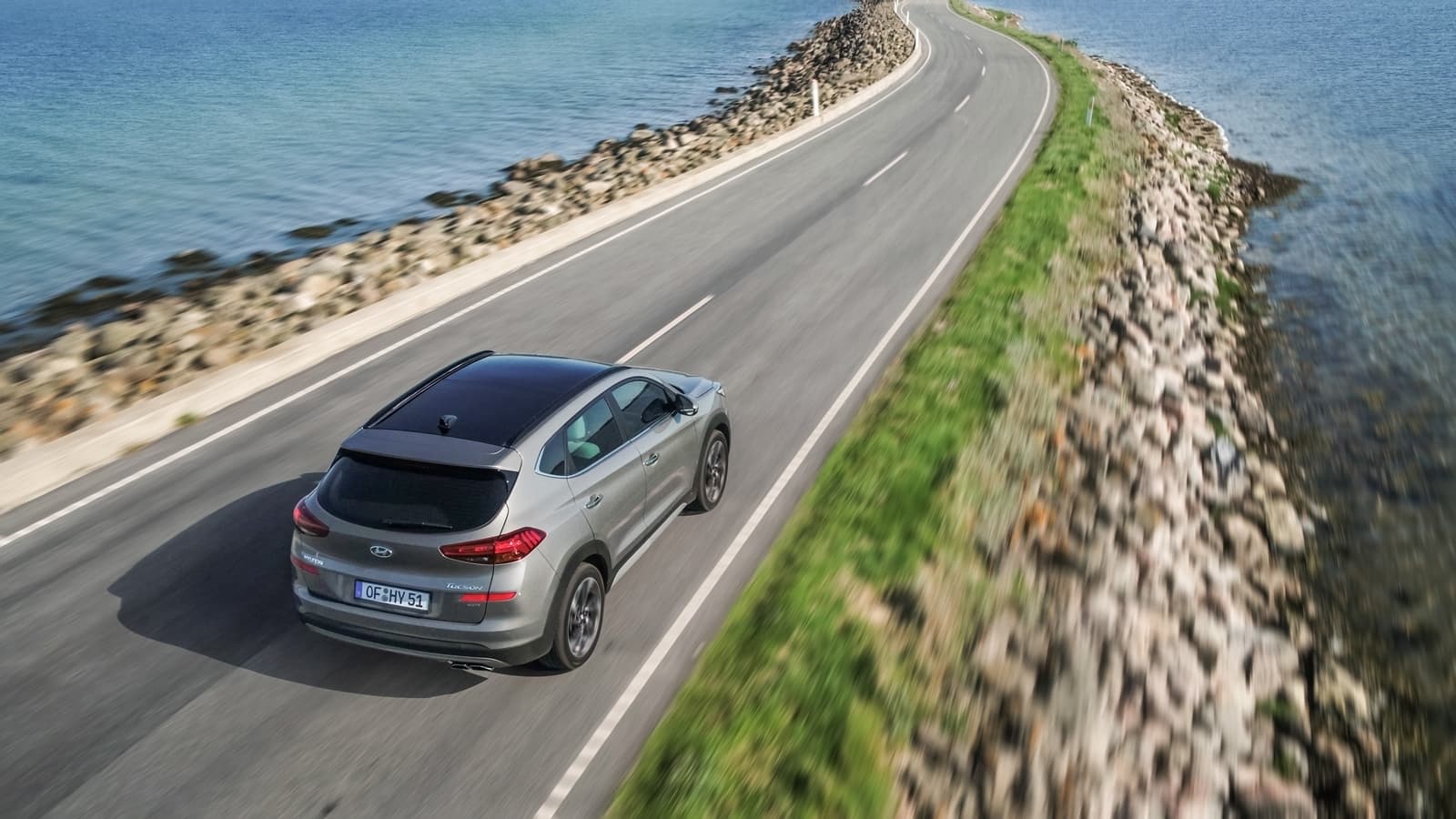 Vista trasera lateral del Hyundai Tucson en movimiento sobre una carretera costera.