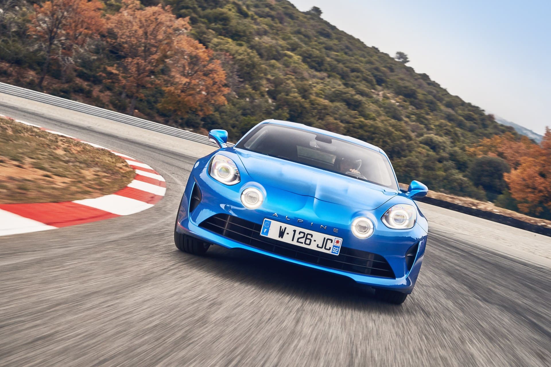 Alpine A110 azul en acción sobre circuito, mostrando su dinámica delantera y lateral.