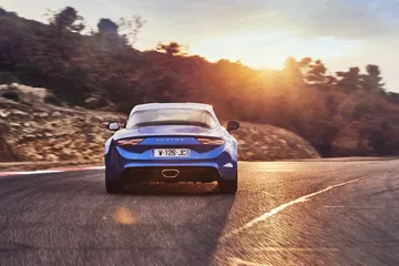 Vista trasera y lateral del Alpine A110 en carretera, mostrando su silueta deportiva.