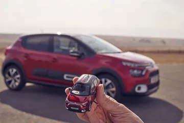 Citroën C3 en rojo, visto lateralmente con un enfoque selectivo y modelo a escala en primer plano