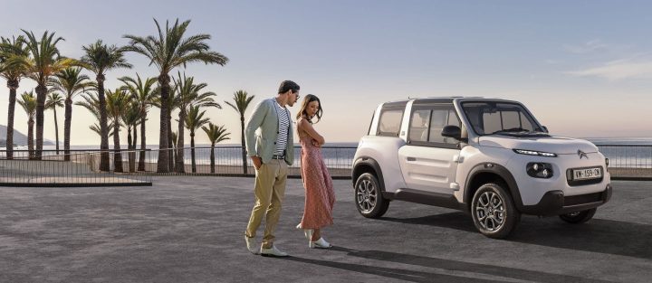Vista lateral del Citroën e-Mehari junto a la playa con una pareja al lado.