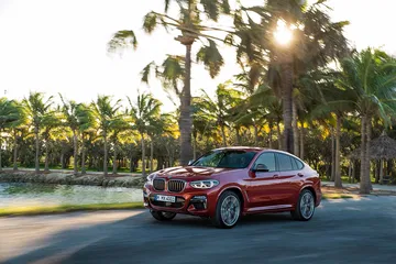 BMW X4 en movimiento con un fondo de palmeras y sol del atardecer.