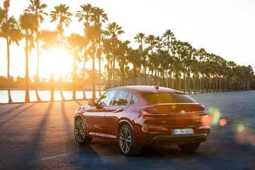 Vista trasera y lateral del BMW X4 al atardecer con un juego de luces y palmeras de fondo.