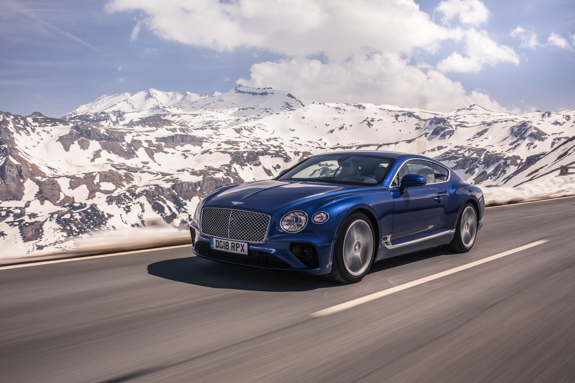 Bentley Continental GT azul recorriendo carretera con paisaje montañoso.