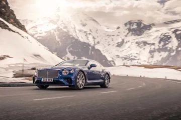 Bentley Continental GT en curva con paisaje montañoso de fondo.
