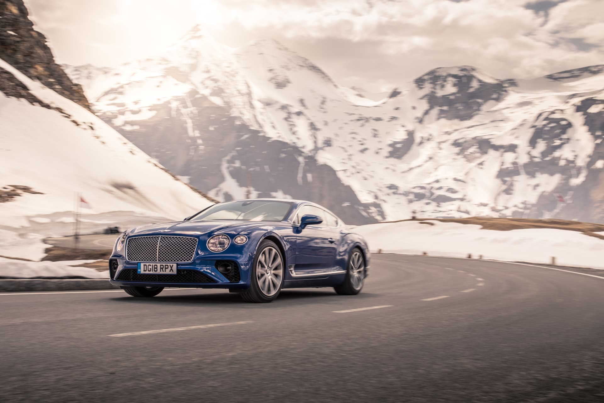Bentley Continental GT en curva con paisaje montañoso de fondo.