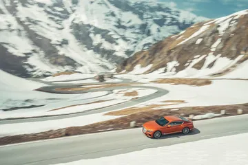 Vista lateral del Bentley Continental GT circulando en carretera de montaña