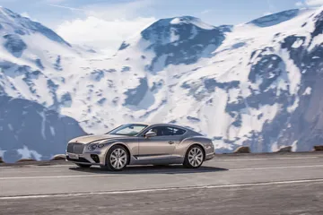 Vista lateral del Bentley Continental GT con montañas nevadas de fondo.