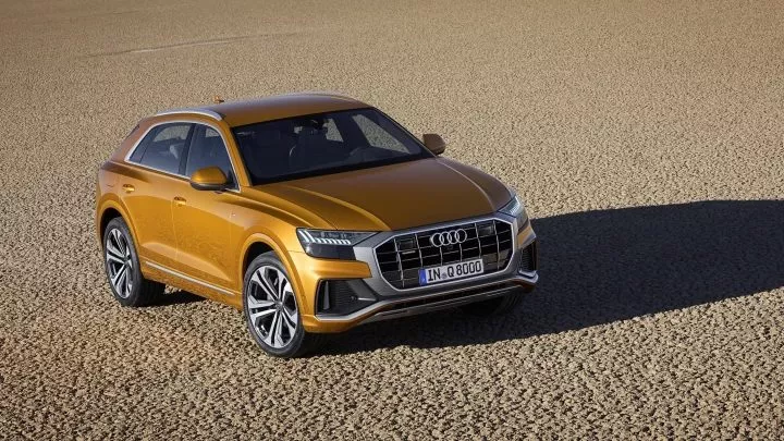 Vista lateral del Audi Q8 en elegante color dorado sobre fondo de arena.