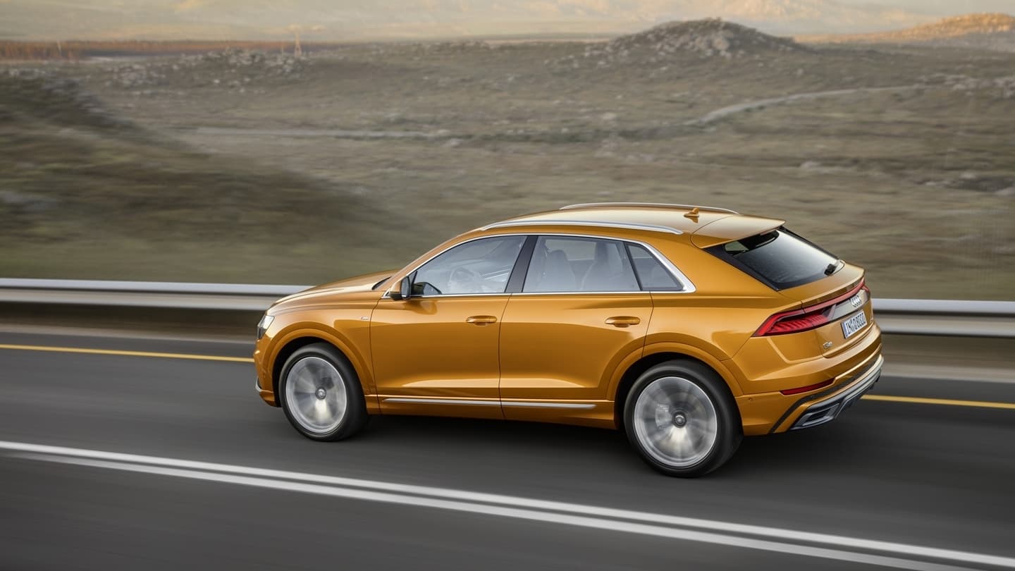 Vista lateral del Audi Q8 en movimiento, destacando su diseño aerodinámico y llantas deportivas.