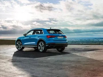 Audi Q3 mostrando su perfil y parte frontal con cielo nublado de fondo.