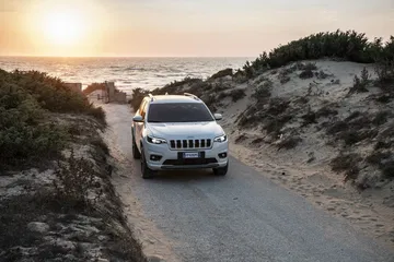 Vista frontal del Jeep Cherokee rodando por caminos arenosos al atardecer.