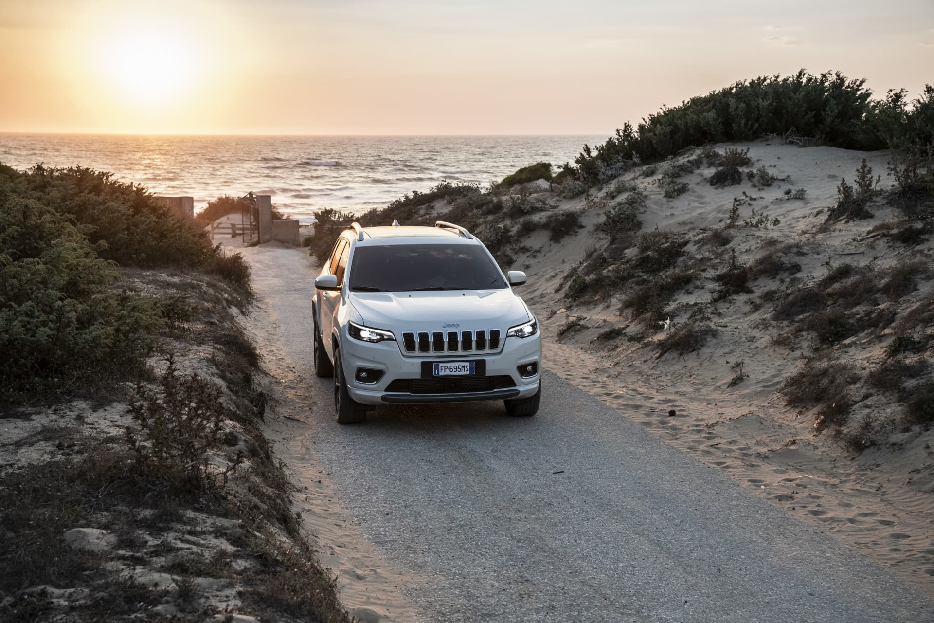 Vista frontal del Jeep Cherokee rodando por caminos arenosos al atardecer.