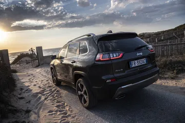 Vista trasera y lateral del Jeep Cherokee en un camino costero al atardecer.
