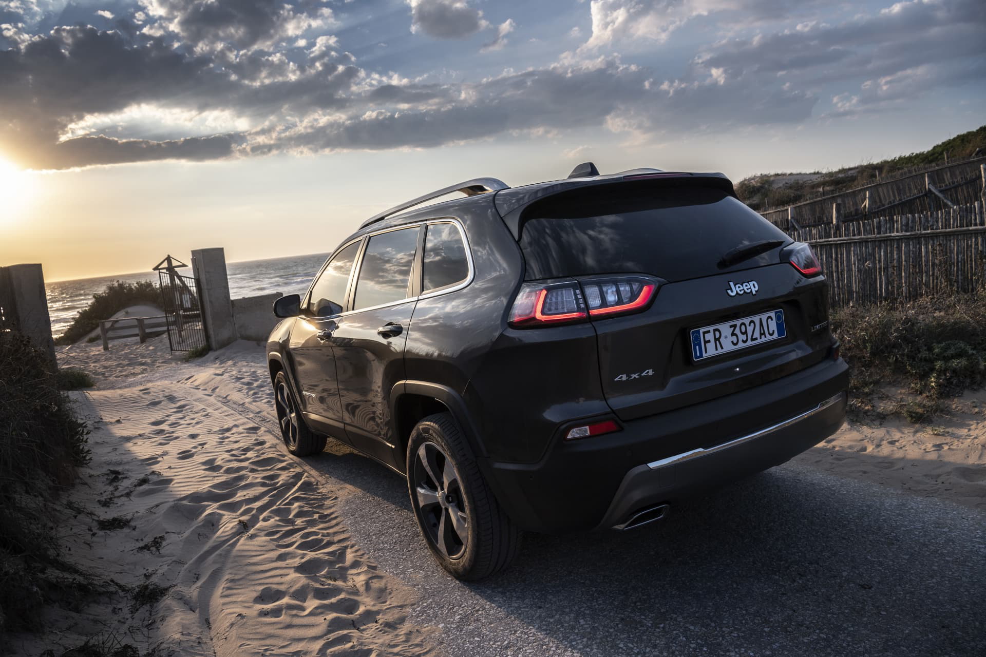 Vista trasera y lateral del Jeep Cherokee en un camino costero al atardecer.