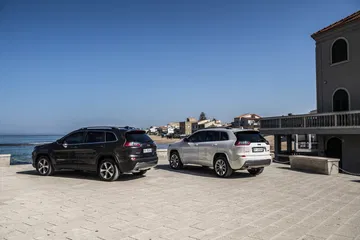 Dos Jeep Cherokee aparcados frente al mar, vista lateral que muestra líneas de diseño.