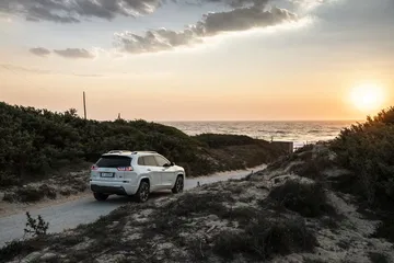 Vista lateral de un Jeep Cherokee en un camino costero al atardecer.