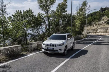Vista angular delantera del Jeep Cherokee en entorno urbano, destacando su robustez.